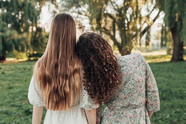 Back view of two young girls standing in the summer city park or forest woods and looking away