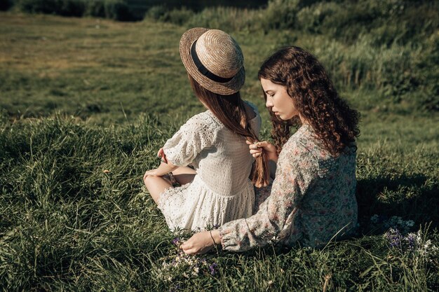 Back view of two young ladies sitting on the grass in the sunny morning summer country