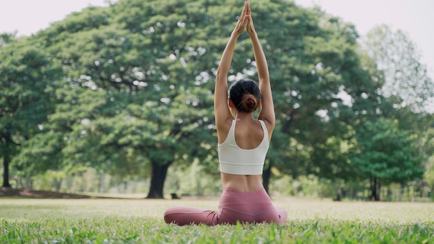 Back view of an unrecognizable slender Asian young woman sitting on the grass in the lotus position