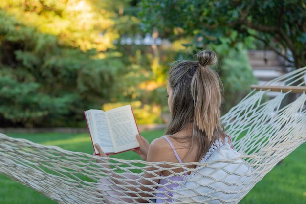 Back view of unrecognizable woman in a camping hammock reading a book as pleasure activity