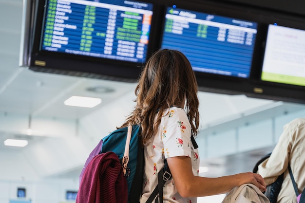 Foto vista posteriore donna irriconoscibile che legge le informazioni sui voli sul tabellone delle partenze all'aeroporto