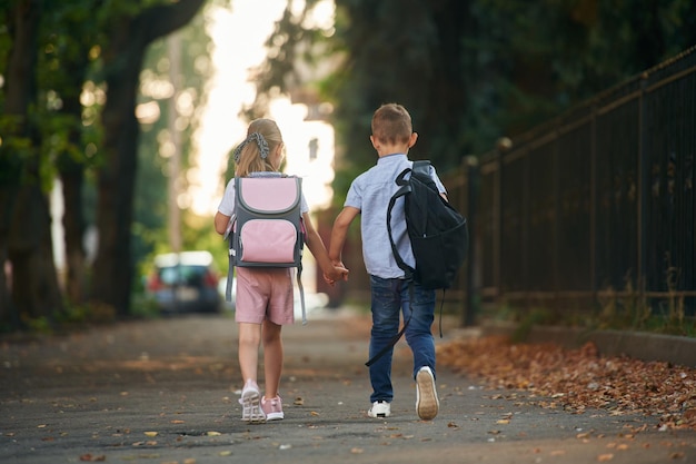 写真 歩いている後ろの景色 男の子と女の子の若い学校の子供たちは外で一緒にいます