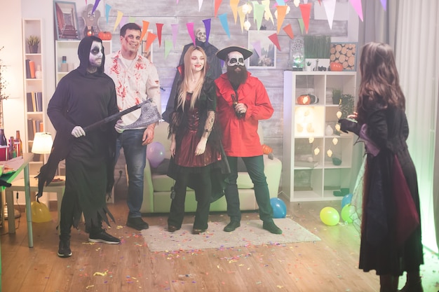 Вид сзади ведьмы, фотографирующей зомби и его друзей на праздновании хэллоуина.