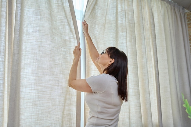 Photo back view woman closes light curtains in the living room