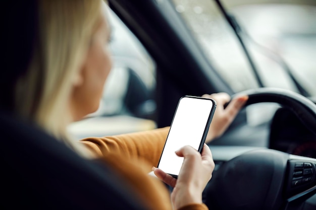 Вид сзади на женщину за рулем автомобиля с телефоном в руках
