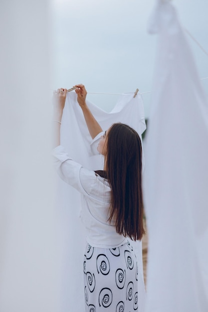 Back view of woman hanging laundry with clothespin on clothesline in nature