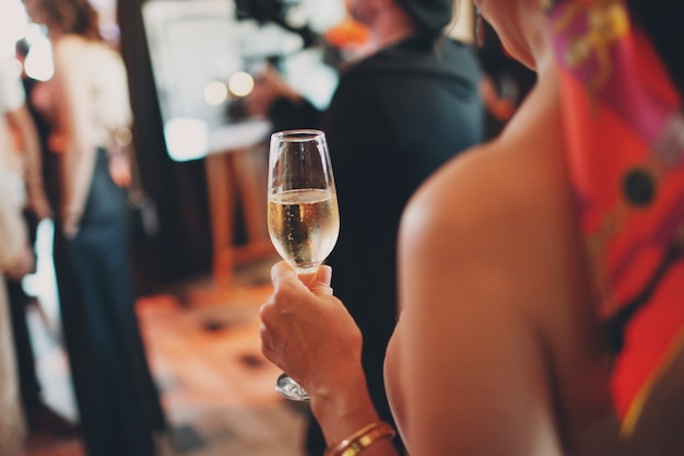 Back view woman holds misted cold glass of champagne wine in hand at party event