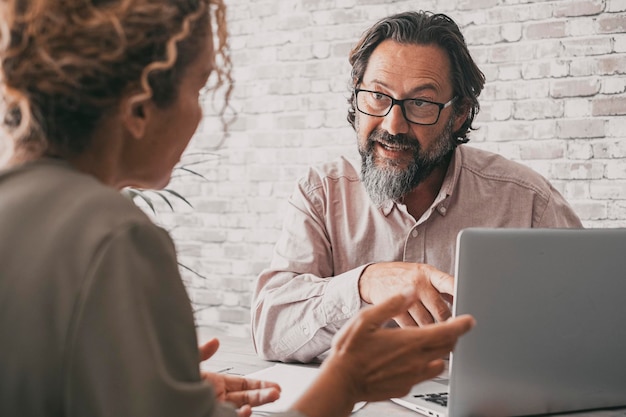 Vista posteriore di donna e uomo in ufficio consulente e cliente seduto alla scrivania parlando e utilizzando il computer portatile professionista al lavoro concetto di stile di vita aziendale e ufficio persone moderne e computer