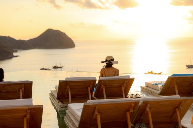 Back view of a woman sitting on relaxing chair enjoying sunset\
and sea view