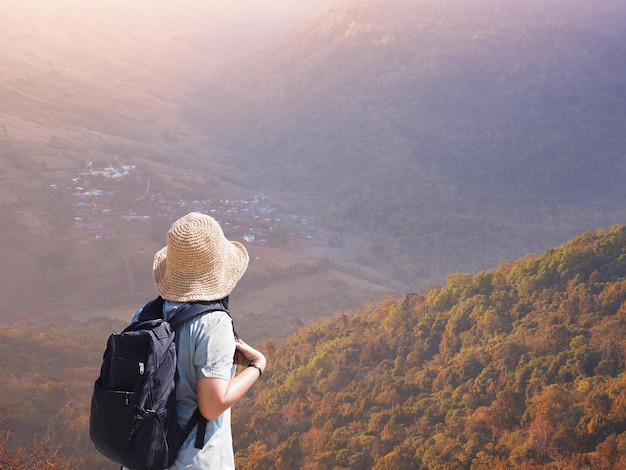 Zaino in spalla turistico della donna di vista posteriore che esamina la foresta di autunno sull'alta montagna