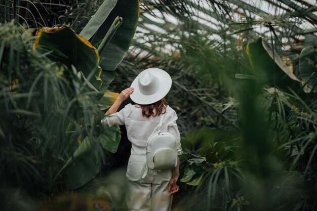 Photo back view of woman tourist in a hat standing in palm greenhouse of botanical garden