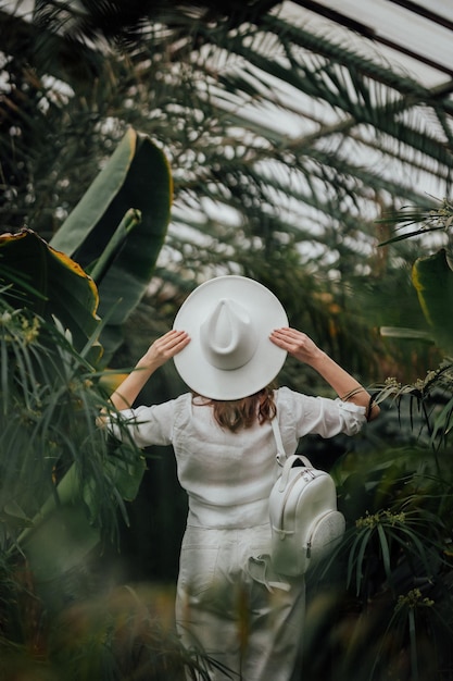 Задний вид женщины-туриста в шляпе, стоящей в пальмовом теплице ботанического сада
