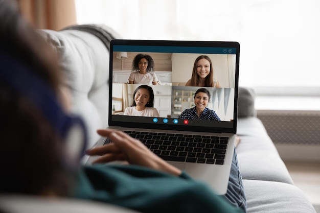 Back view of woman use laptop talk speak on video call with multiracial female friends or colleagues Female relax have webcam digital conference on computer engaged in online meeting with coworkers