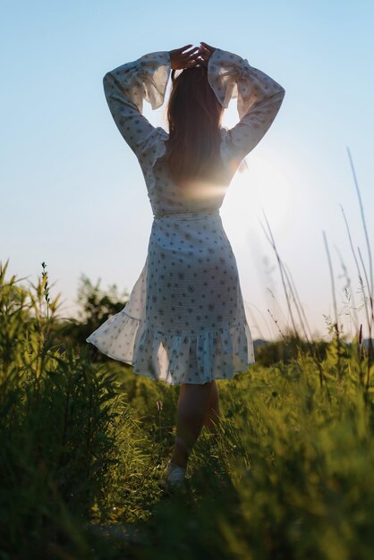 Photo back view of a woman in a white dress in a field at sunset