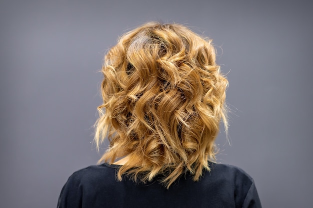 Back view of the woman with long brown curly hair stands on a dark background.