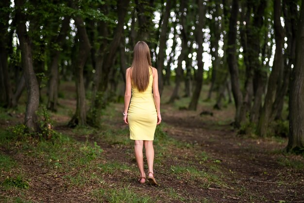 Back view of a woman in yellow dress standing in moody dark forest.