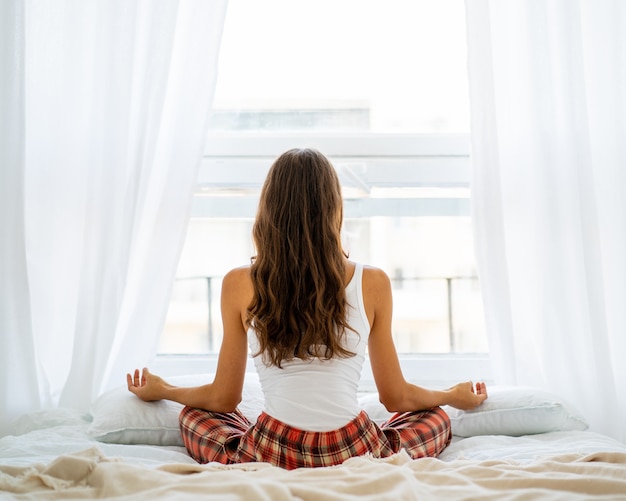 Vista posteriore della posa di yoga della donna a letto dopo il risveglio, entrando nel nuovo giorno