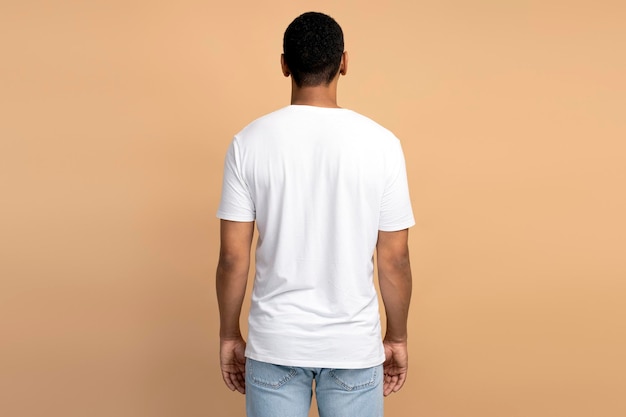 Back view of a young adult brunette man standing over the beige wall background