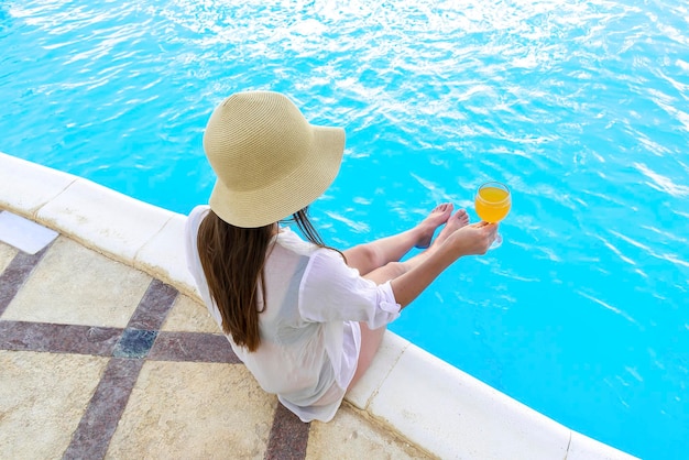 Back view young adult female woman person enjoy relaxing on\
swimming pool edge in luxury hotel resort outdoor looking on blue\
clear water summer travel tropical recreational vacation tourism\
concept