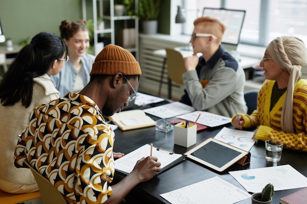 Vista posteriore al giovane uomo di colore che prende appunti nell'incontro con il team di business creativo in ufficio