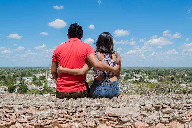 Back view of young couple looking at the outskirts of the city from the heights in Ermita de Tekax