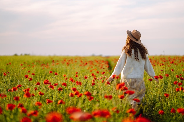 後ろ姿 ケシ畑でポーズをとる帽子をかぶった巻き毛の若い女性夏の風景