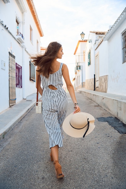 Вид сзади молодой элегантной женщины в соломенной шляпе, ходить по узким улочкам старого города.