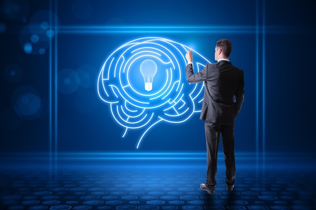 Back view of young european male using abstract digital light bulb with human brain inside glowing on blurry blue background Creative innovation and inspiration Business and Technology idea concept