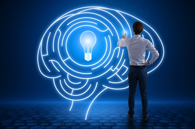 Back view of young european man using abstract digital light\
bulb with human brain inside glowing on blurry blue background\
creative innovation and inspiration business and technology idea\
concept