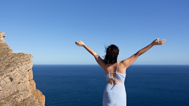 Back view of a young female enjoying freedom with hands raised