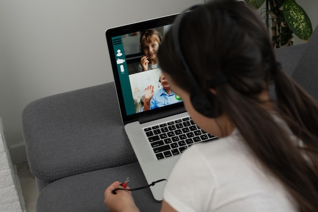 Back view of young girl sit at home, talk have online video\
call lesson with teacher or tutor, teenage schoolgirl engaged in\
webcam conversation, study distant use web conference app on\
laptop