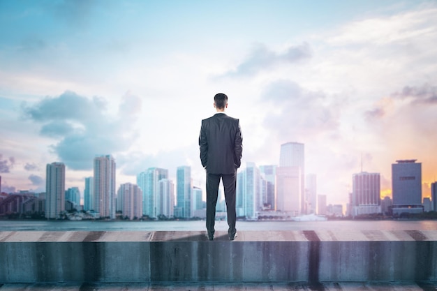 Back view of young male standing on concrete edge of building on city background with mock up place in sky Success future vision and leadership concept