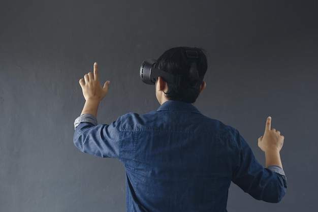 Back view of young man in casual style wearing virtual reality googles his finger pointing out or t