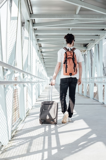 空港で灰色の荷物と手をつないで、旅行の概念、飛行機に乗る、急いで若い男の背面図