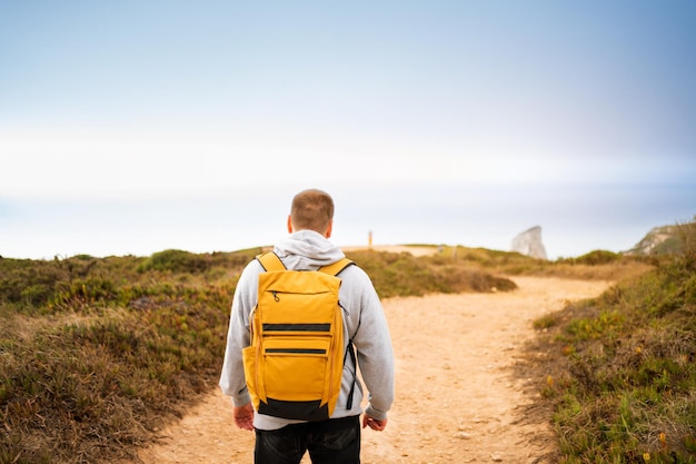 Back view young man traveler with yellow backpack