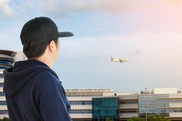 Back view of young man wearing a black cap and long sleeve blue looking to the airplane