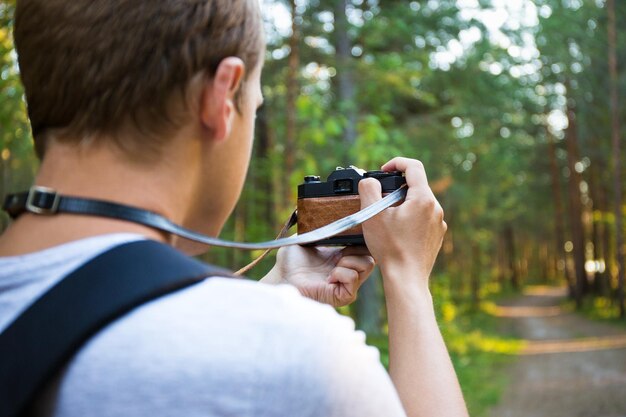 Вид сзади на молодого человека с рюкзаком, фотографирующегося в лесу
