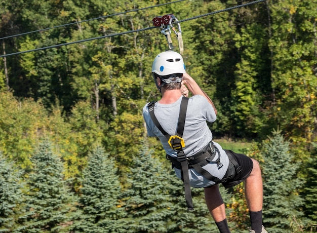 Back view of young man on zip line harness riding the zipline\
down between trees