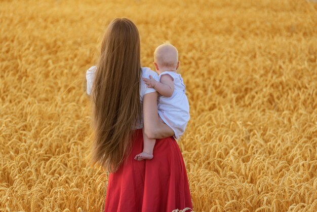 Back view of young mother with beautiful hair holding baby. Mother and child in wheat field