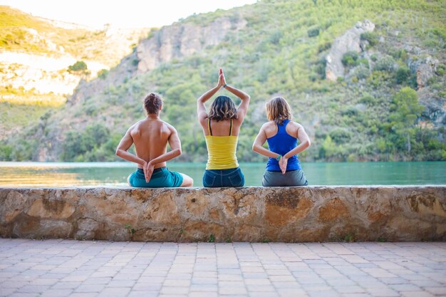 Back view of young people sitting on wall towards a lake