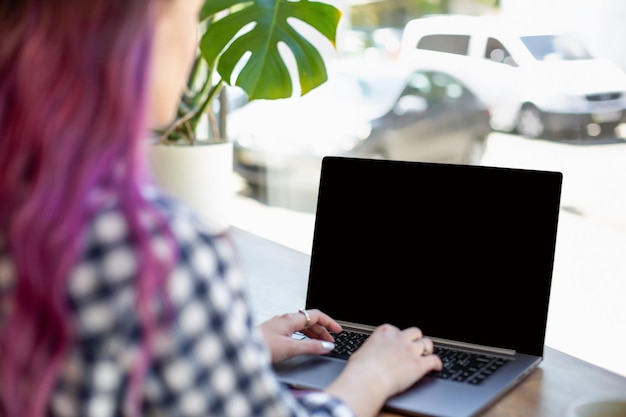 Вид сзади молодой женщины с розовыми волосами, играющей на портативном компьютере с пустой копией космического экрана, ...