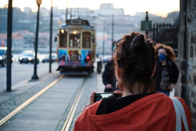 Back view of a young traveler taking a picture of a tram in the city during the daytime