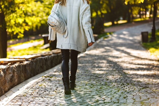 Foto vista posteriore di una giovane donna vestita in cappotto di autunno e cappello che cammina all'aperto in strada della città