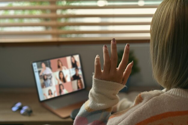 Back view of young woman having video conference with colleagues on computer laptop