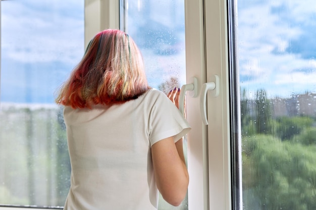 Back view of young woman looking out rainy summer window