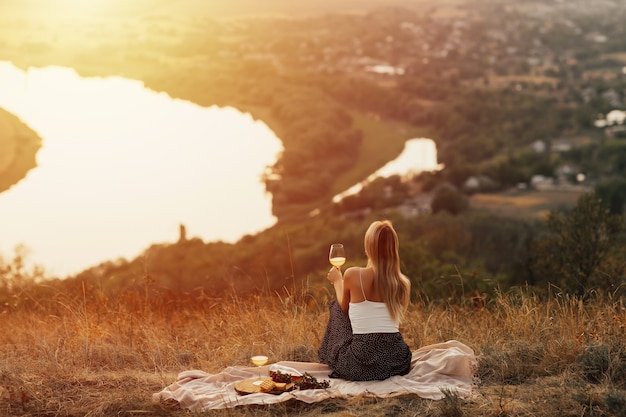 リラックスして秋の夕日を楽しんでいる若い女性の背面図。自然のピクニックの女性。
