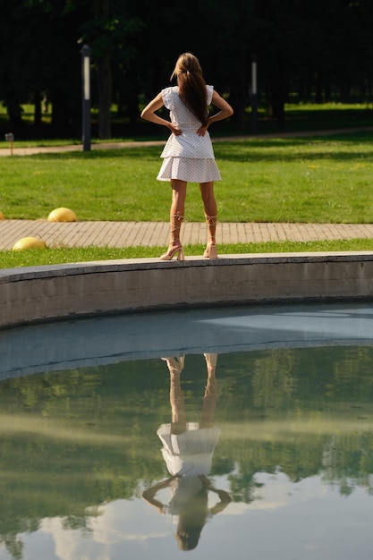 Back view of young woman standing the curb of the city fountain in the park