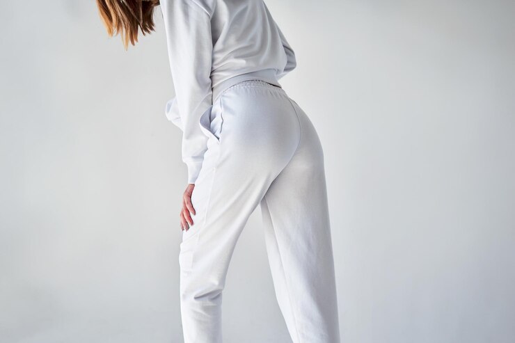 Photo 白いミニマリストのスウェットパンツを着た若い女性の後ろの景色 白い衣装で快適に歩いて カジュアルなエレガンス スポーツウェアモックアップ 白いズボンを着た女の子