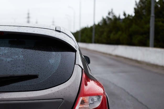 Back window of grey car parked on the street in autumn rainy day, rear view.