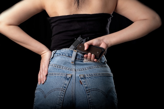黒の表面にピストル銃を保持している女性の1つの手、拳銃を運ぶ若いセクシーな女の子、きれいな女性が銃を持って立つ